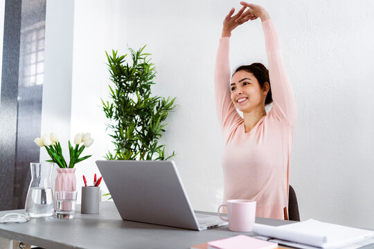 Young woman with hand raised using laptop while sitting at home office