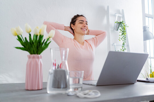 Young woman with hands behind head smiling while sitting at home office