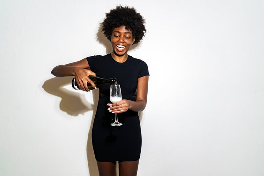 Happy young woman pouring champagne in champagne flute while standing against white background