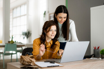 Smiling daughter with mother looking at laptop while sitting at desk in home office