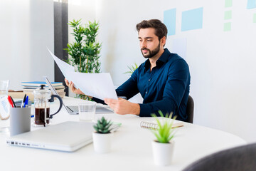 Male entrepreneur looking at documents while sitting against wall in office