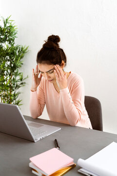 Young woman with head in hands sitting by laptop on table at home office