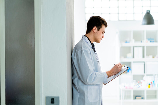 Male medical professional writing notes while standing against wall in hospital