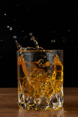 Close-up of crystal glass with whiskey splashing on wooden table, on black background, in vertical, with copy space