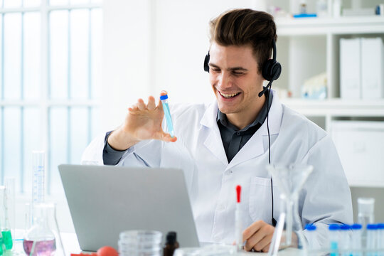 Smiling young scientist showing test tube during video call on laptop in laboratory