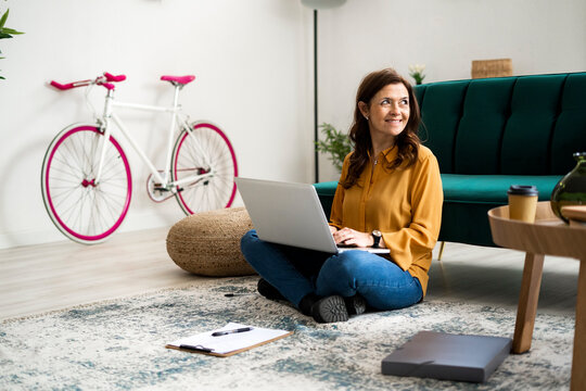 Smiling woman with laptop looking away while sitting on floor at home