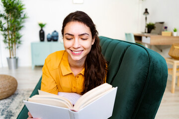 Young woman reading book while lying on sofa at home