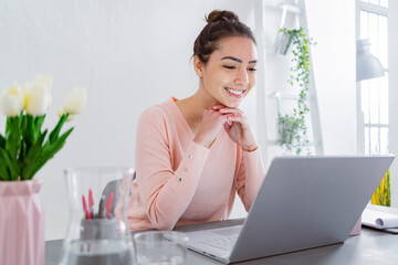 Young woman with hand on chin using laptop while talking with friend on laptop at home
