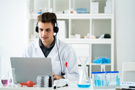 Young male scientist with headphones during video call on laptop in laboratory
