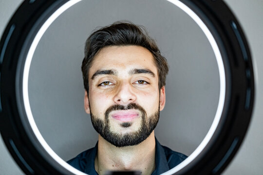 Handsome Man Seen Through Illuminated Ring Light Against Gray Wall