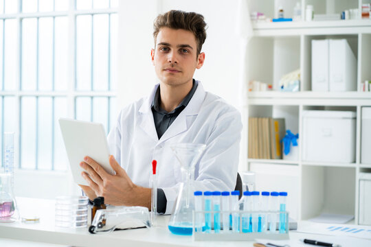 Young male scientist holding digital tablet while sitting at desk in laboratory