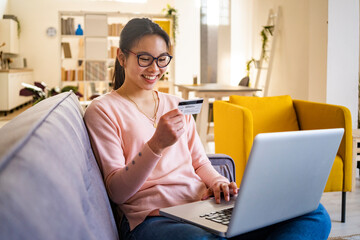 Happy woman sitting with credit card and laptop at home