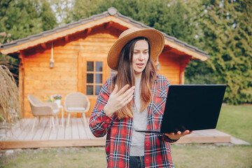 Blogger working on laptop in the garden, Young gardener greets someone over the internet on a laptop. Woman with a computer in hand. Gardening with fun.	