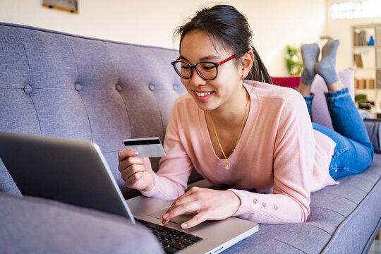 Young woman with credit card smiling while using laptop at home