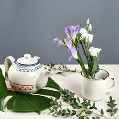 white teapot and cup on white wood background with green leaf and purples, white flowers background gray