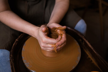 dirty hands of a person make a product out of clay on a machine in a room
