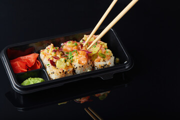 Fresh sushi rolls with shrimp, crab served in lunch box for takeaway. To go Japanese sushi food concept for healthy lunch. Closeup view on black background.