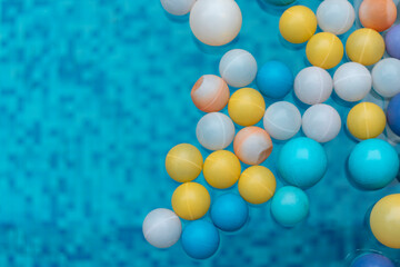 Plastic balls of various sizes in blue, white, orange and yellow, floating on the pool water.