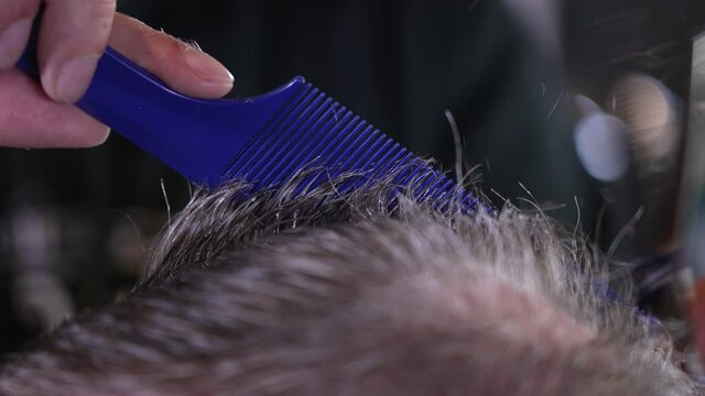 A slow motion close up view of a barber cutting a gentleman's hair.  	