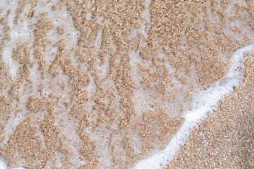 Sea waves and white bubbles, lapping on the sand.