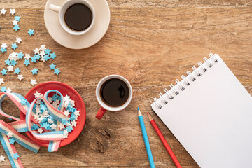 Coffee cup, candies, antistress toy in the form of American flag, blank notebook paper, pencils on a wooden background. Independence Day, 4th of July celebration concept.