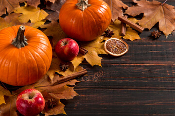 Orange pumpkins, fallen leaves, apples, nuts, spices and cones on a wooden background. The concept...