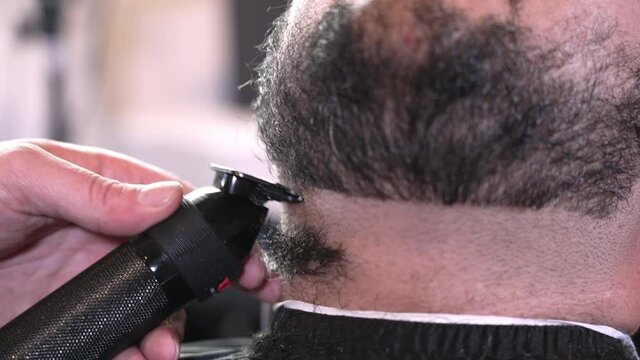 A closeup view of a barber trimming a man's beard and neckline.  	