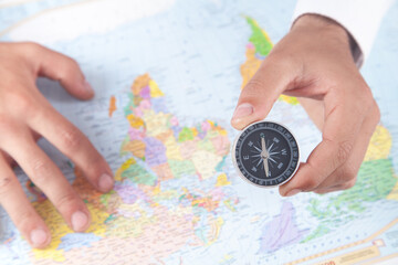 Male hand showing compass on the world map background.