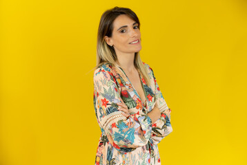 Caucasian woman in summer dress with arms folded isolated over yellow background.