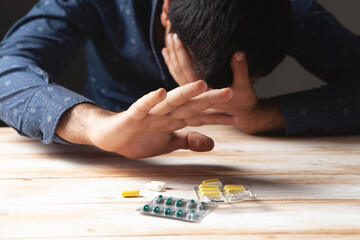 Drug abuse: Young man sitting on a table, drugs and pills in front of him
