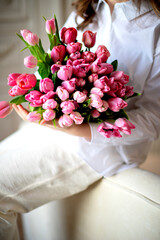 A huge beautiful bouquet of pink tulips in the hands of a girl in a white shirt and cream trousers