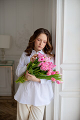 A beautiful little girl in a white shirt with long curly brown hair and blue eyes holds a huge bouquet of Tulips in her hands