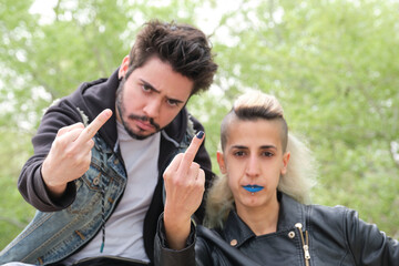 Young punk couple flipping the bird to the camera in a park. Rock and roll lifestyle.