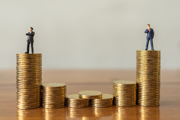 Business Money and Financial Concept. Two businessman miniature figures people standing on top of stack of gold coin on wooden table.