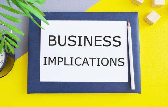 Business implications text memo written on a white paper above Notebook with pencil. Business concept