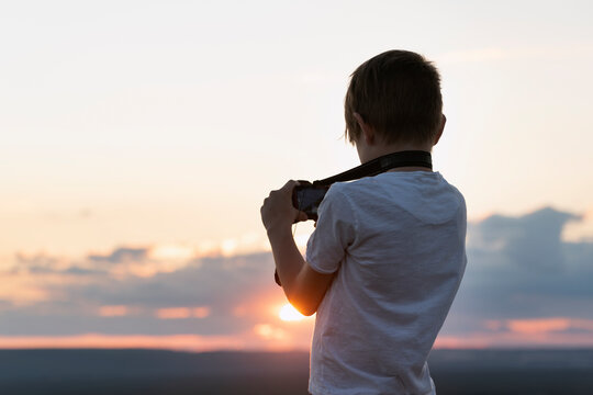 Boy photographs the sunset. Child with camera on setting sun background.