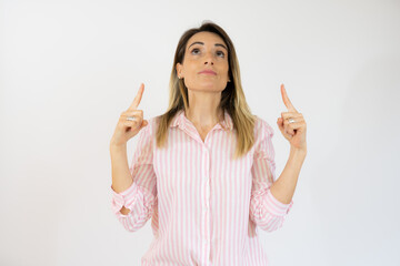 Smiling woman in casual shirt pointing fingers up isolated over white background.