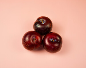 three delicious and Juicy Red Plums on a Pink Background 