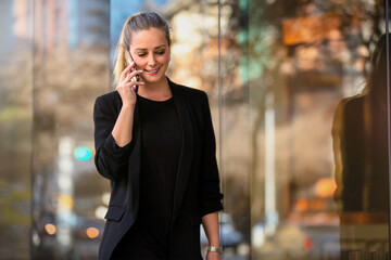 Candid lifestyle portrait of stylish female business woman talking on a cellphone while walking in city with a cheerful smile
