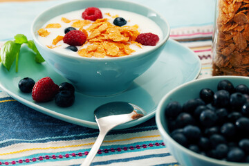 Breakfast of cornflakes and raspberries, blueberries and milk in a blue plate