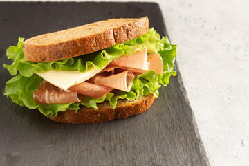 sandwich with ham, cheese and lettuce leaves on a cutting board. Home cooking