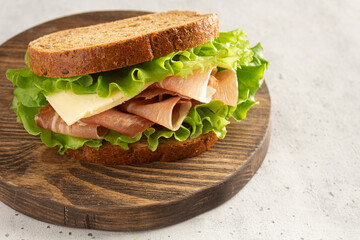 sandwich with ham, cheese and lettuce leaves on a cutting board. Home cooking