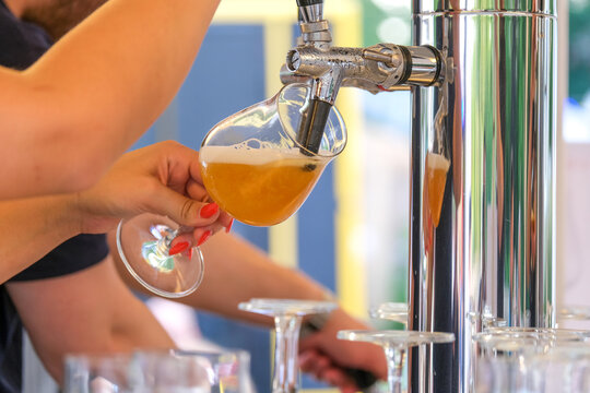 Nahaufnahme: Junge Kellnerin zapft ein frisches Bier an der Theke draußen, während ein Kollege im Hintergrund Gläser spült, selektiver Fokus