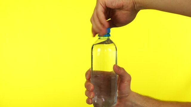 Man hand is opening a blue bottle of fresh water on yellow background isolated on yellow background