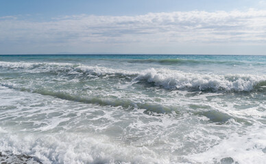 Summer sunny day on the Mediterranean coast. Rest, vacations, travel. Stormy sea with white waves and foam against the blue sky. Horizontal photo. 