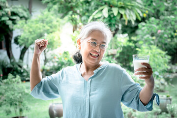 An Asian elderly woman, happy and showing her strength In good health, and holding a glass of milk...