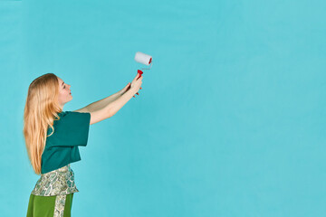 Artist woman painting the wall. Cute female painter painting the wall. Young girl in casual clothes with roller drawing or writing on empty wall.