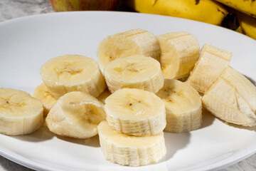 A bunch of bananas and a sliced banana on a plate on a table. Selective focus.
