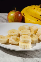A bunch of bananas, a sliced banana, and an apple on a plate on a table. Selective focus