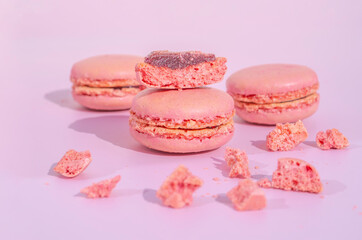 Tasty pink raspberry macarons on light violet background. French homemade dessert with small broken pieces